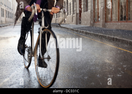 Businessman riding bicycle in rainy street Stock Photo