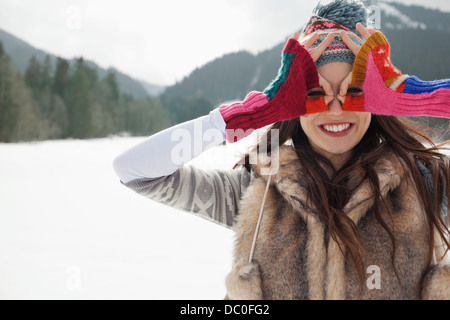 Portrait of smiling woman circling eyes with fingers in snowy field Stock Photo