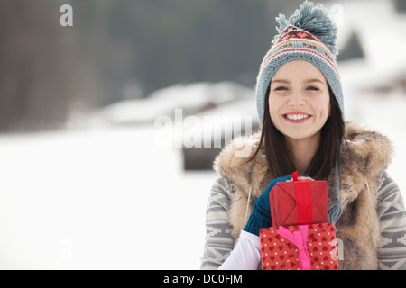 Portrait of smiling woman with Christmas gifts in snowy field Stock Photo