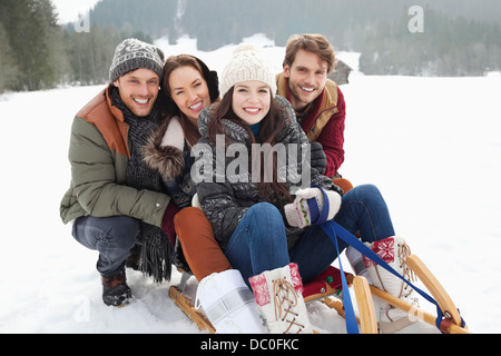 Portrait of happy friends on sled in snowy field Stock Photo
