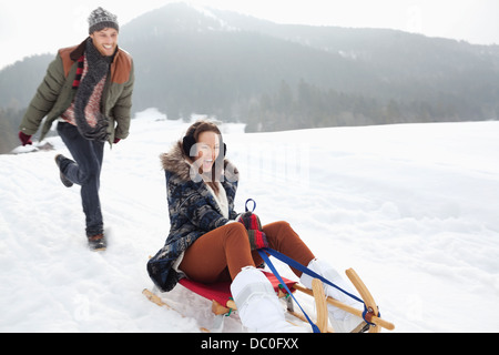 Enthusiastic couple sledding in snowy field Stock Photo