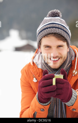 Close up portrait of smiling man in knit hat and gloves drinking coffee in snowy field