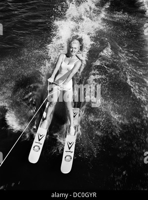 1950s 1960s HIGH ANGLE VIEW SMILING BLOND WOMAN IN WHITE ONE PIECE BATHING SUIT WATER SKIING Stock Photo