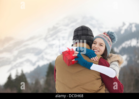 Happy woman holding gift and hugging man with mountains in background Stock Photo