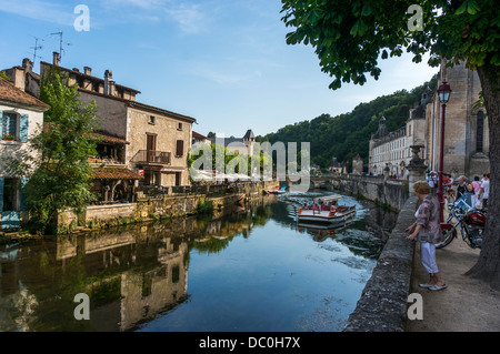 River Dronne, with a passing tour boat and the abbey and people keeping to the shade, in Brantôme, in the Dordogne in south west France, Europe. Stock Photo