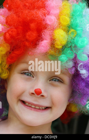 a close up of a cute, smiling toddler boy dressed up in a costume clown wig and face paint Stock Photo