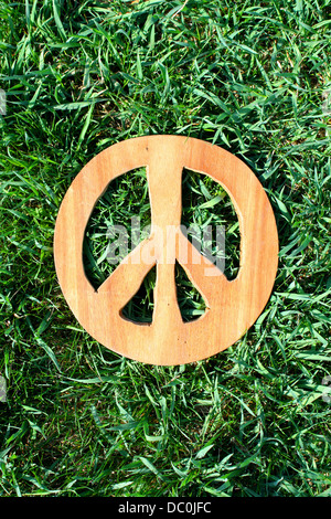 A wooden, hand carved peace sign laying in the green grass. Stock Photo
