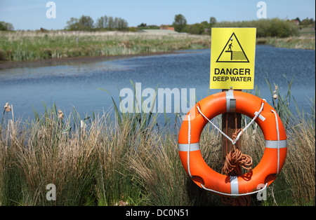 A Danger Deep Water sign in present along with a Lifering / Lifebouy in front of a deep lake. Stock Photo