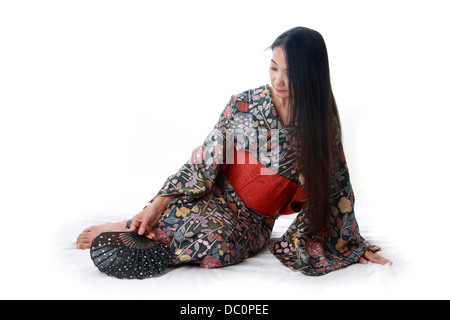 Japanese Lady Sitting on the Floor Wearing a Traditional Blue and Red Patterned Kimono and Holding a Fan
