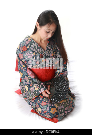 Japanese Lady Sitting on the Floor Wearing a Traditional Blue and Red Patterned Kimono and Holding a Fan