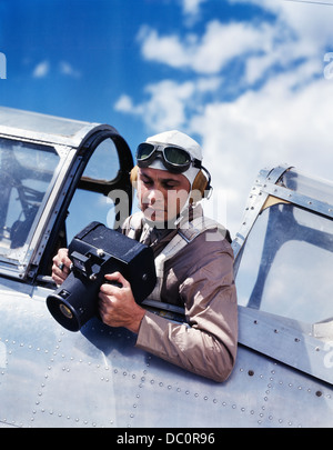 1940s ARMY AIR CORPS MAN SITTING AIRPLANE COCKPIT WEARING FLYING GOGGLES HELMET PARACHUTE TAKING PHOTOGRAPHS WITH AERIAL CAMERA Stock Photo