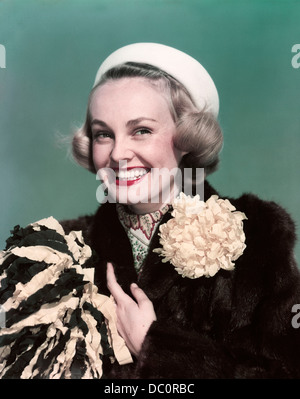 1940s 1950s PORTRAIT SMILING BLOND WOMAN WEARING FUR COAT WITH MUM FLOWER DECORATION HOLDING POMPOM Stock Photo