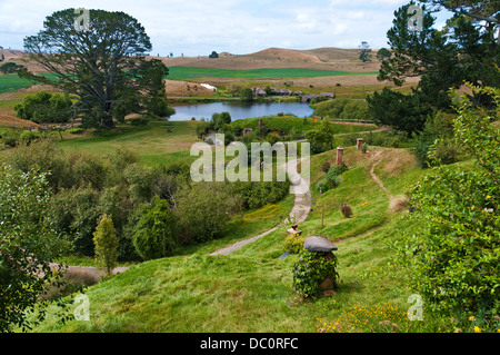 Very green Hobbiton with meandering path through image with lake and Party tree in background, showing hobbit hole chimneys