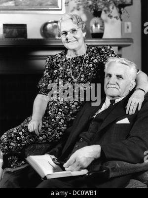 1940s PORTRAIT SMILING SENIOR COUPLE MAN WOMAN SITTING IN EASY CHAIR LOOKING AT CAMERA Stock Photo