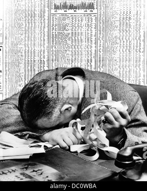 1940s MAN HEAD ON DESK HOLDING STOCK TICKER TAPE WITH NEWSPAPER STOCK PAGE BEHIND HIM Stock Photo