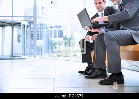 Businessmen sharing laptop in lobby Stock Photo