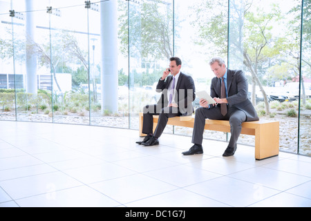 Businessmen using cell phone and digital tablet in lobby Stock Photo
