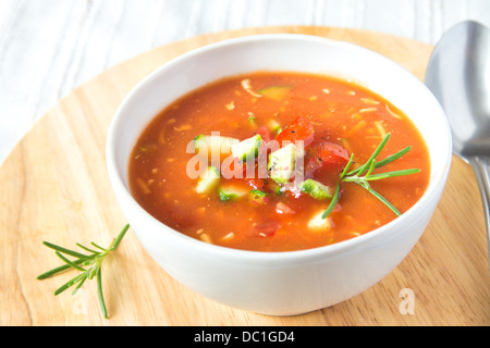 Fresh delicious tasty cold tomato soup gazpacho in white bowl with spoon on wooden board, closeup, horizontal Stock Photo