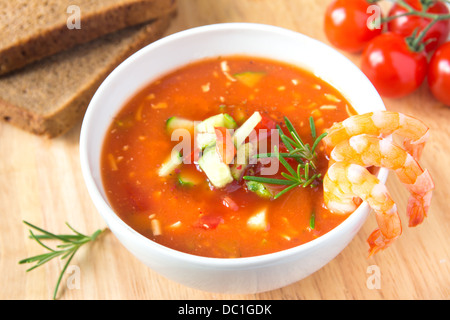 Fresh delicious tasty cold tomato soup gazpacho with shrimps in white bowl with spoon on wooden board, closeup, horizontal Stock Photo