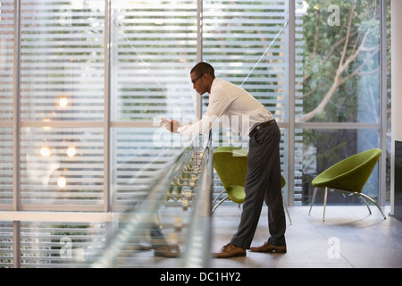 Businessman leaning on railing in office and text messaging with cell phone Stock Photo