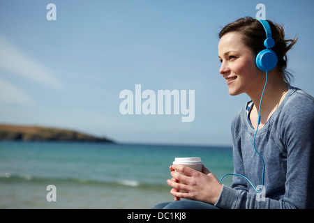 Young woman at coast with coffee and earphones