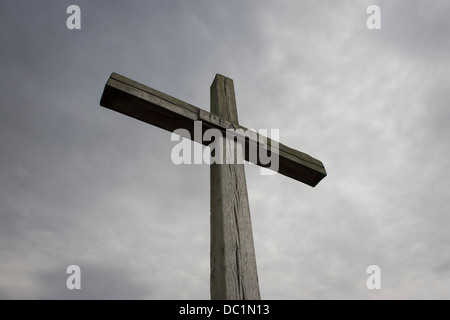 A cross made from English oak rises up into threatening grey English skies. With splits in its vertical and horizontal beams, the word Peace is written in lettering in the centre in an image of Christian values - a message for mankind, of humanity and goodwill to all Men. The wood is from the royal estate of Sandringham in Norfolk, presented in August 1987 by Queen Elizabeth II to mark the site of the high altar of the former St Benet's Abbey near Ludham on the Norfolk Broads. Stock Photo