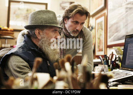 Senior and mid adult man using laptop in antique shop Stock Photo