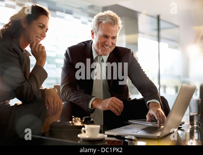 Smiling businessman and businesswoman using laptop in lobby Stock Photo