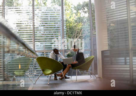 Businessman and businesswoman using laptop in lobby Stock Photo