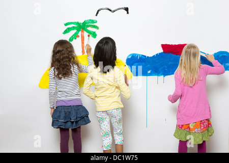 Three girls painting ocean and island on wall Stock Photo