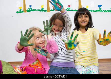 Three girls kneeling on floor with painted hands Stock Photo