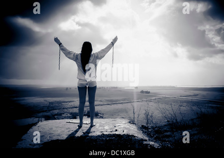 Woman wearing chains and straitjacket looking out over land Stock Photo