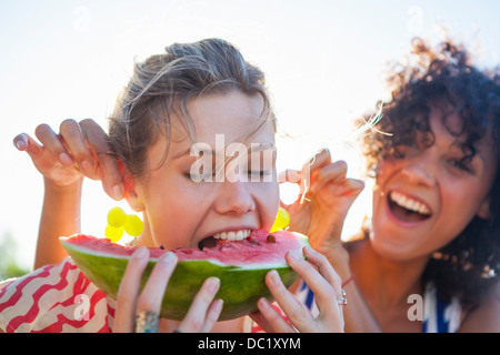 Young woman eating watermelon as friend pulls her ears Stock Photo