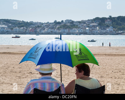 Couple sitting on Instow beach using an umbrella as a parasol, North Devon, England Stock Photo