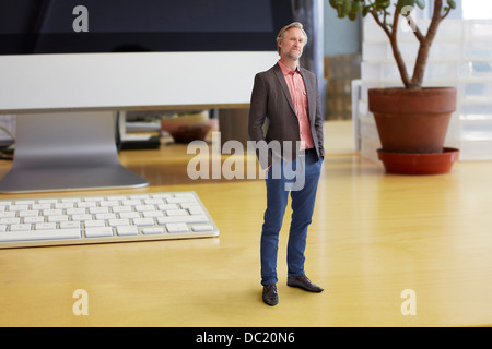Mature businessman standing on oversized desk Stock Photo