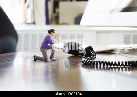Businesswoman shouting through large telephone receiver on oversized desk Stock Photo