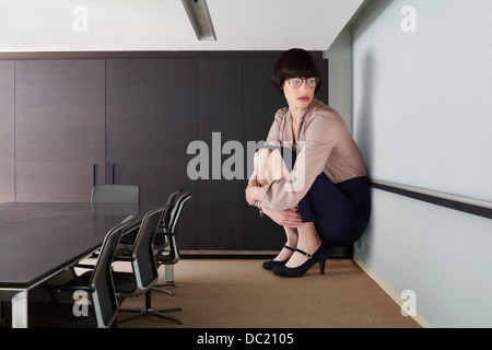 Businesswoman crouching in small conference room Stock Photo