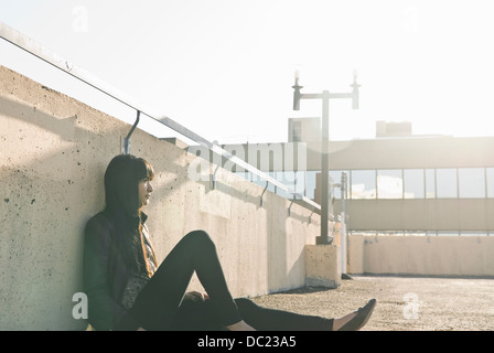 Young woman sitting on sunlit rooftop Stock Photo
