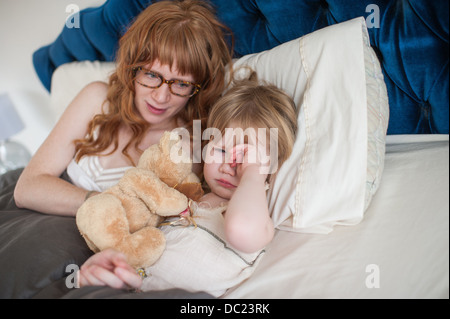 Girl rubbing eyes in bed, mother comforting Stock Photo