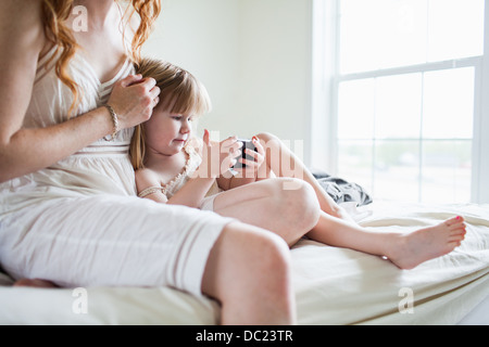 Woman and girl sitting on bed looking at smartphone Stock Photo
