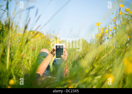 Boy lying in long grass playing on smartphone Stock Photo