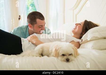 Pregnant woman and partner lying on bed with dog Stock Photo