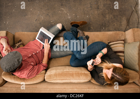 Couple sitting on sofa using digital tablet and smartphone Stock Photo