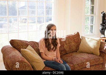 Teenage girl sitting on sofa, smiling Stock Photo