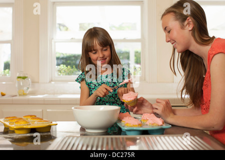 Young girl with older sister icing cupcakes Stock Photo