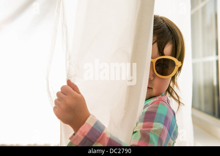 Girl peering round curtain wearing sunglasses Stock Photo