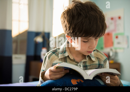 Boy sitting on bed reading book Stock Photo