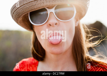 Mature woman wearing sunglasses and sunhat sticking out tongue Stock Photo