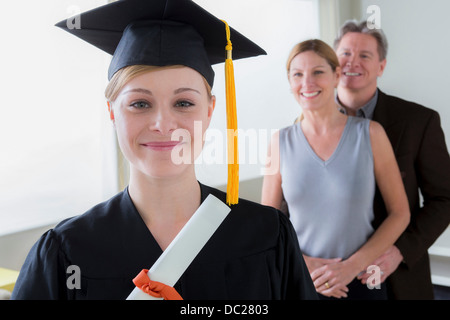 Teenage girl wearing mortarboard with parents in background Stock Photo
