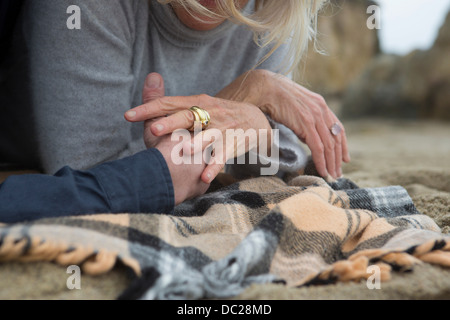 Mature couple lying on beach holding hands, close-up Stock Photo